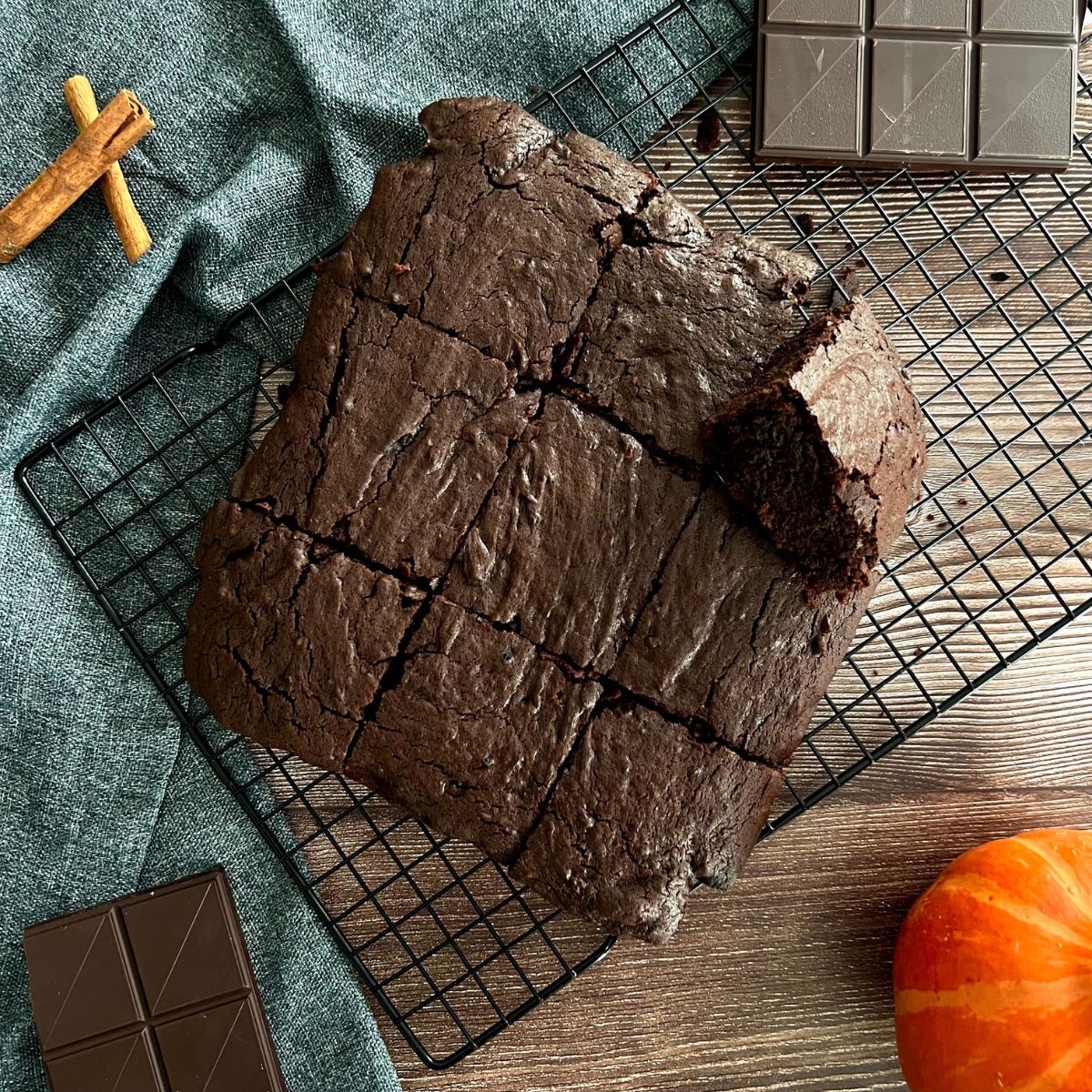 Ein ganzer Brownie Kuchen liegt angeschnitten in neun Teile auf einem Abkühlgitter. Daneben liegt ein Kürbis.