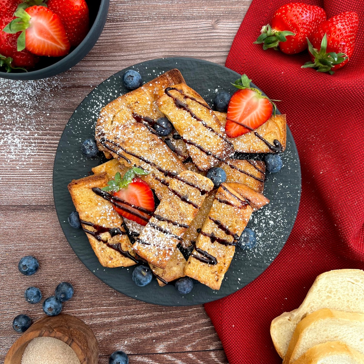 Auf dem Teller liegen French Toast serviert mit Blaubeeren, Erdbeeren und Schokoladensauce.