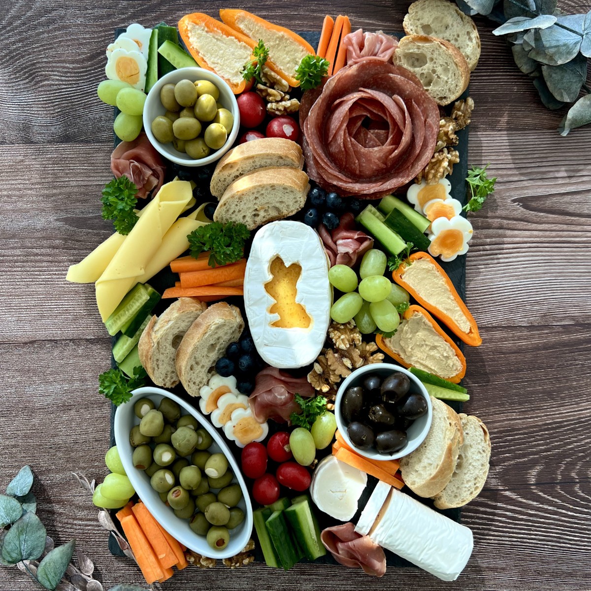 Viele einzelne Zutaten eines Brunches auf einem Teller, in der mitte ein käse mit Hasenmotiv darauf