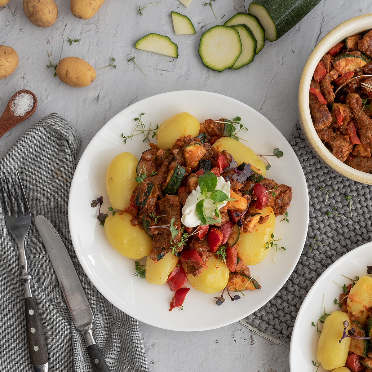 Rindfleisch-Gemüsepfanne mit Rindfleischstreifen und frischem Gemüse wie Paprika, Zucchini und Kartoffeln, angerichtet auf einem weißen Teller, umgeben von Deko.