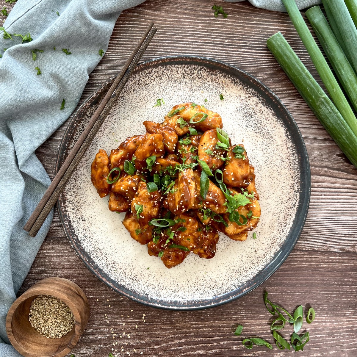 Auf einem flachen Teller liegen gehäuft die Korean Fried Chicken Stücke. Sie sind mit Sesam und Frühlingszwiebel getoppt.