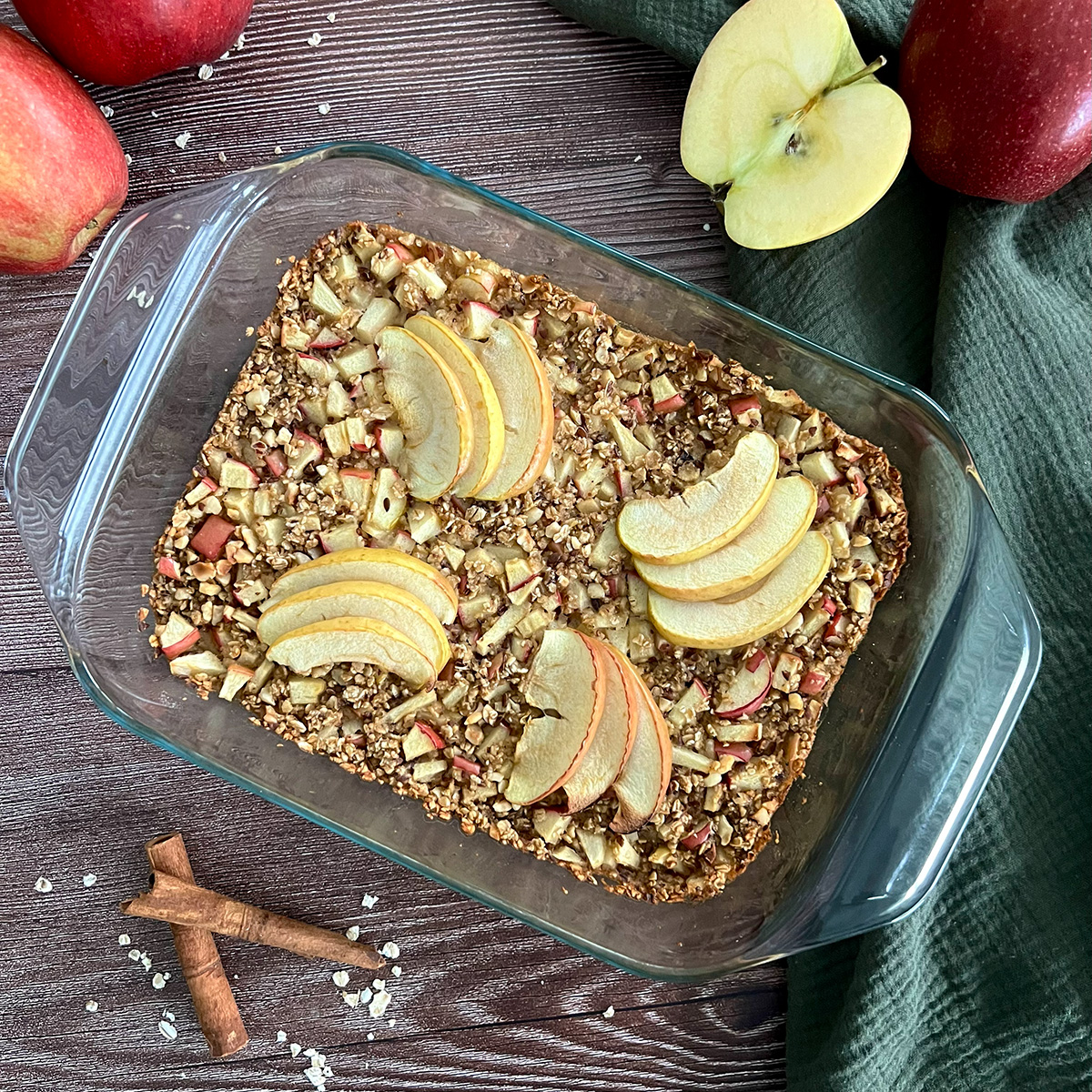 Apfelauflauf in einer Auflaufform daneben Zimt und Äpfel