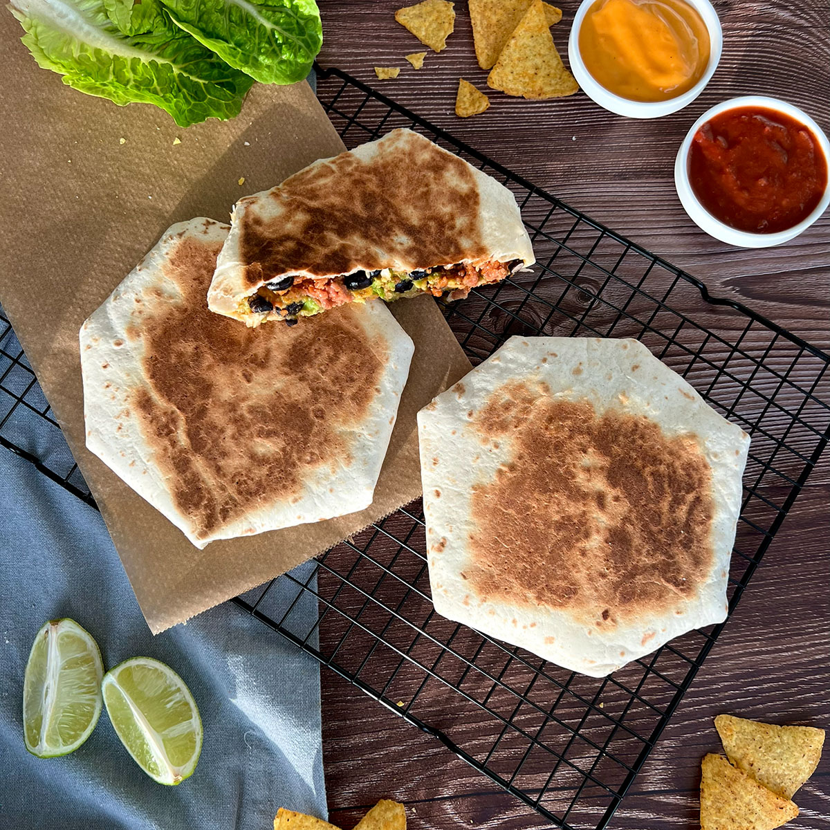 zweieinhalb Wraps auf einem Gitter, daneben Saucen, Salat und andere Toppings