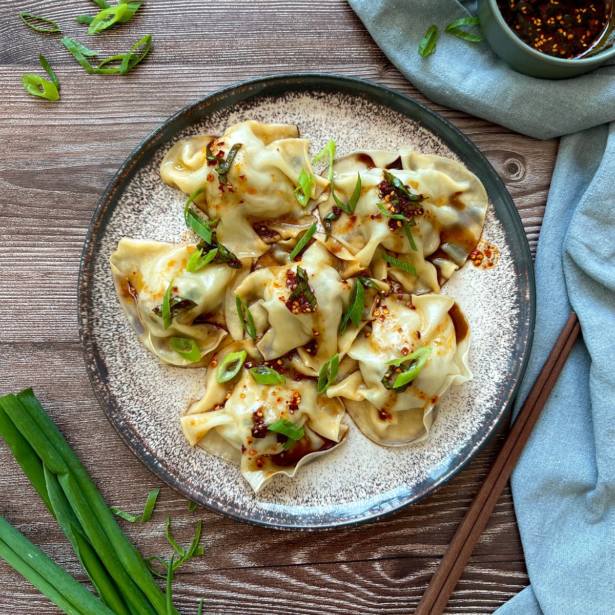 Sechs lazy Dumplings liegen auf einem runden Teller. Mit Frühlingszwiebel und Chilisauce getoppt.