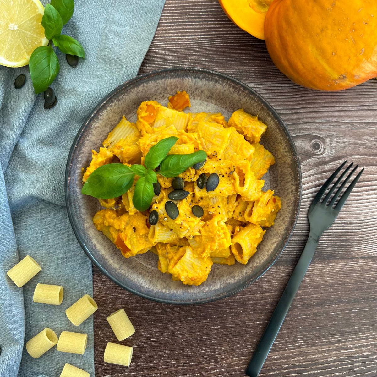 Kürbis Pasta getoppt mit Basilikum und Kürbiskernen in einer schwarzen Schale. Gabel dazu und ein Kürbis liegt daneben.