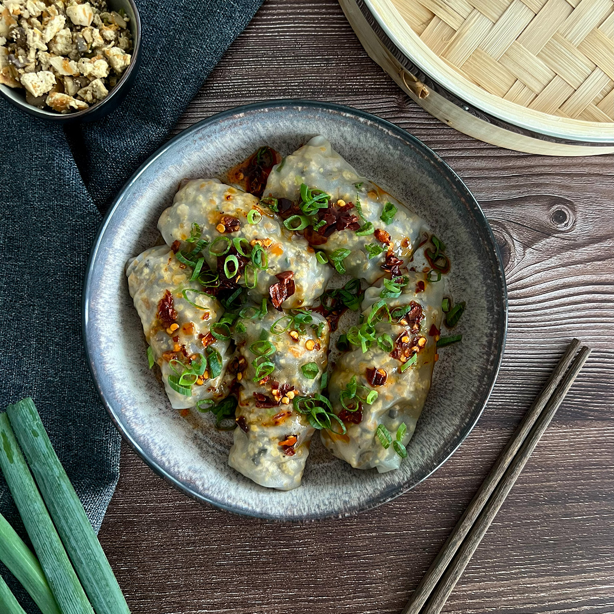 Reispapierdumplings in einer schüssel, daneben Stäbchen und frühlingszwiebeln
