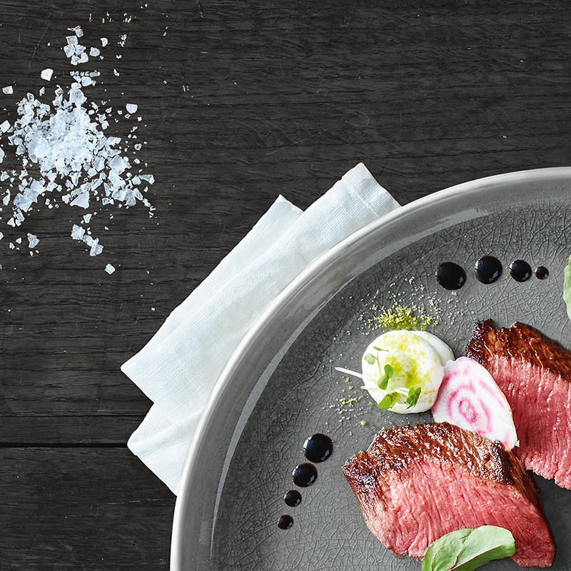 Ein Gericht symbolisch für die Feine-Küche mit gebratenem Fleisch, begleitet mit einer cremigen Beilage und kleinen, rosa-violetten Gemüse-Scheiben.