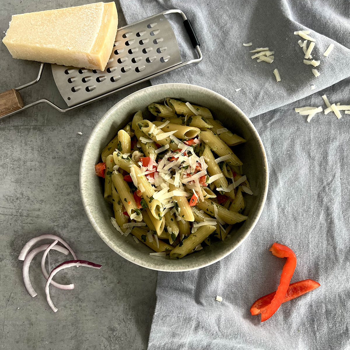 Das Bild zeigt eine tiefe Schale mit der Pasta bestehend aus Spinat, Hähnchen, Paprika und Zwiebeln drin. Serviert mit Parmesan.
