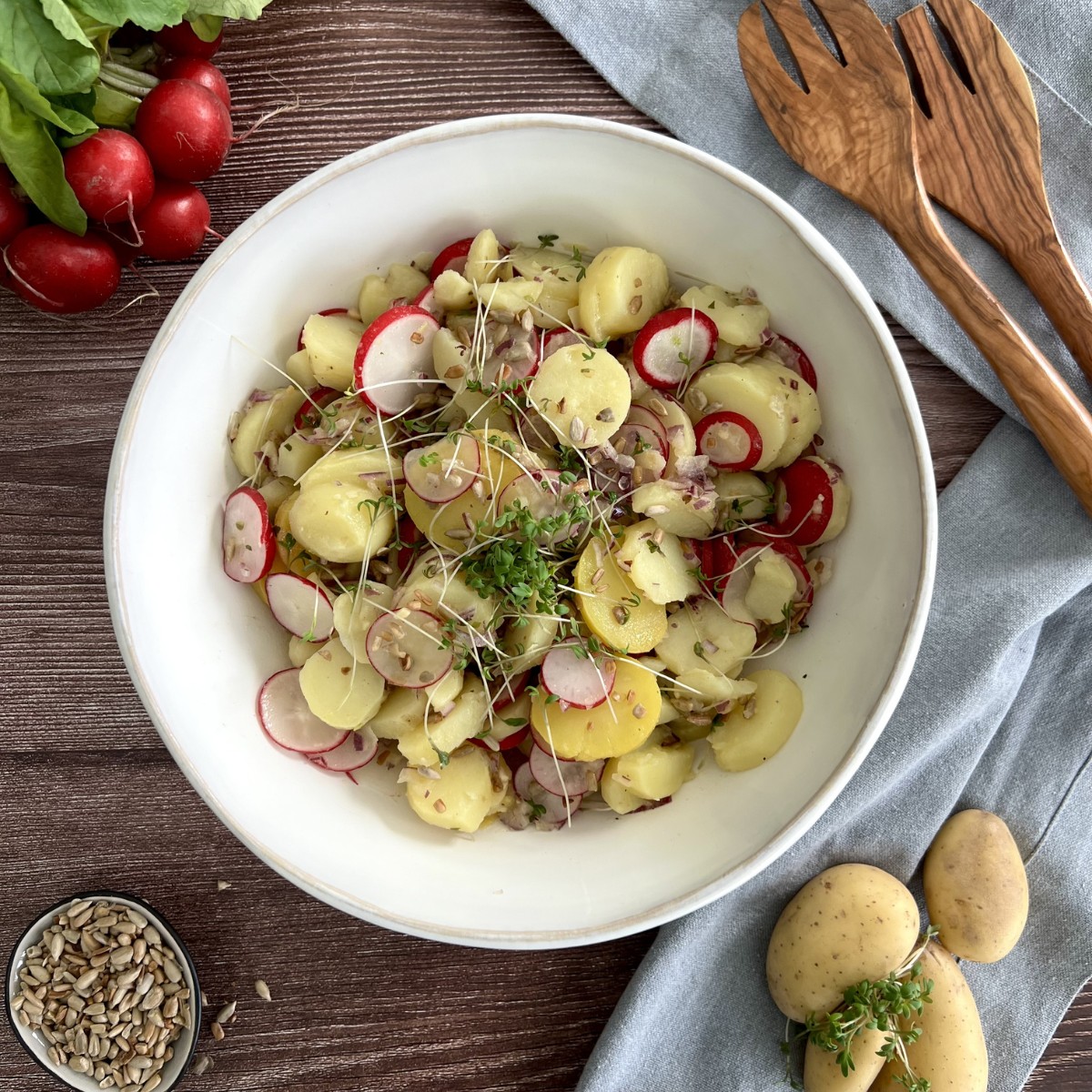 Kartoffel Radieschen Salat in einer großen weißen Salatschüssel getoppt mit Kresse und Sonnenblumenkernen.