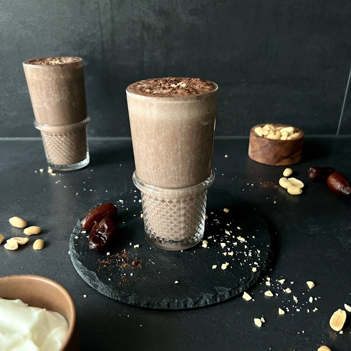 Das Bild zeigt zwei Schokosmoothies zur Deko liegen rund rum Erdnüsse