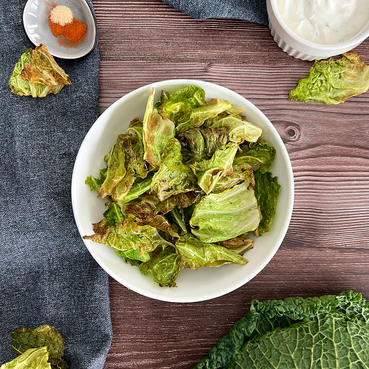 wirsingchips in einer weißen schüsssel, daneben wirsing und ein dip