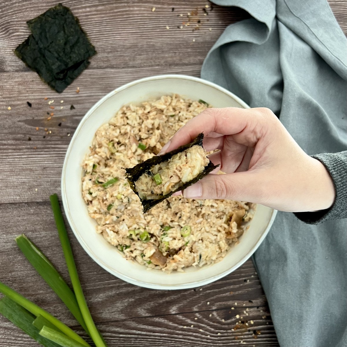 In der Mitte des Bildes steht eine Schale mit der Thunfisch Füllung. Oberhalb der Schale ist eine Hand zu sehen in der die Thunfisch Füllung im Norisnack zu sehen ist.