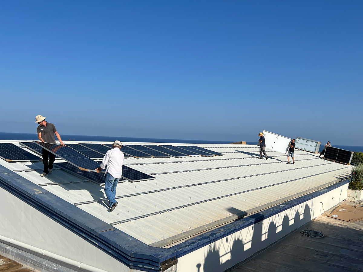 Zwei Männer tragen große Photovoltaik-Panele auf ein Hallendach.
