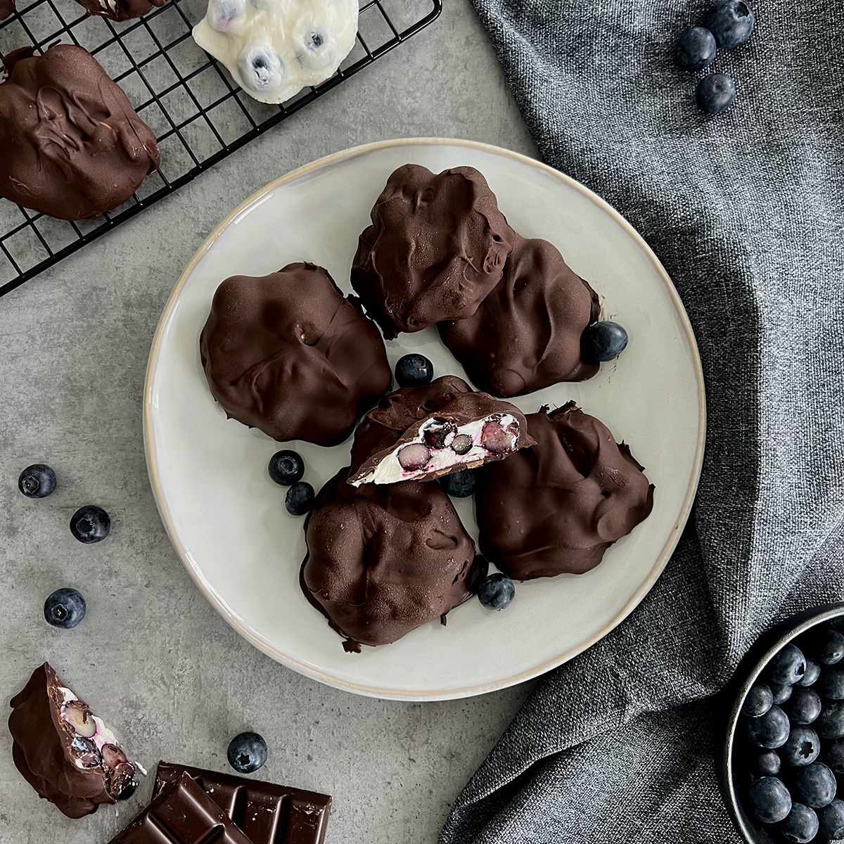 Frozen Joghurt Bites mit Blaubeeren Das Bild zeigt Frozen Joghurt Bites überzogen mit Schokolade und gefüllt mit Blaubeeren. Mehrere liegen auf einem weißen Teller.