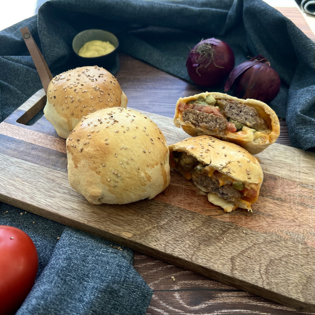 Zwei geschlossener Burger und ein angeschnittener Burger auf einem Holzbrett.