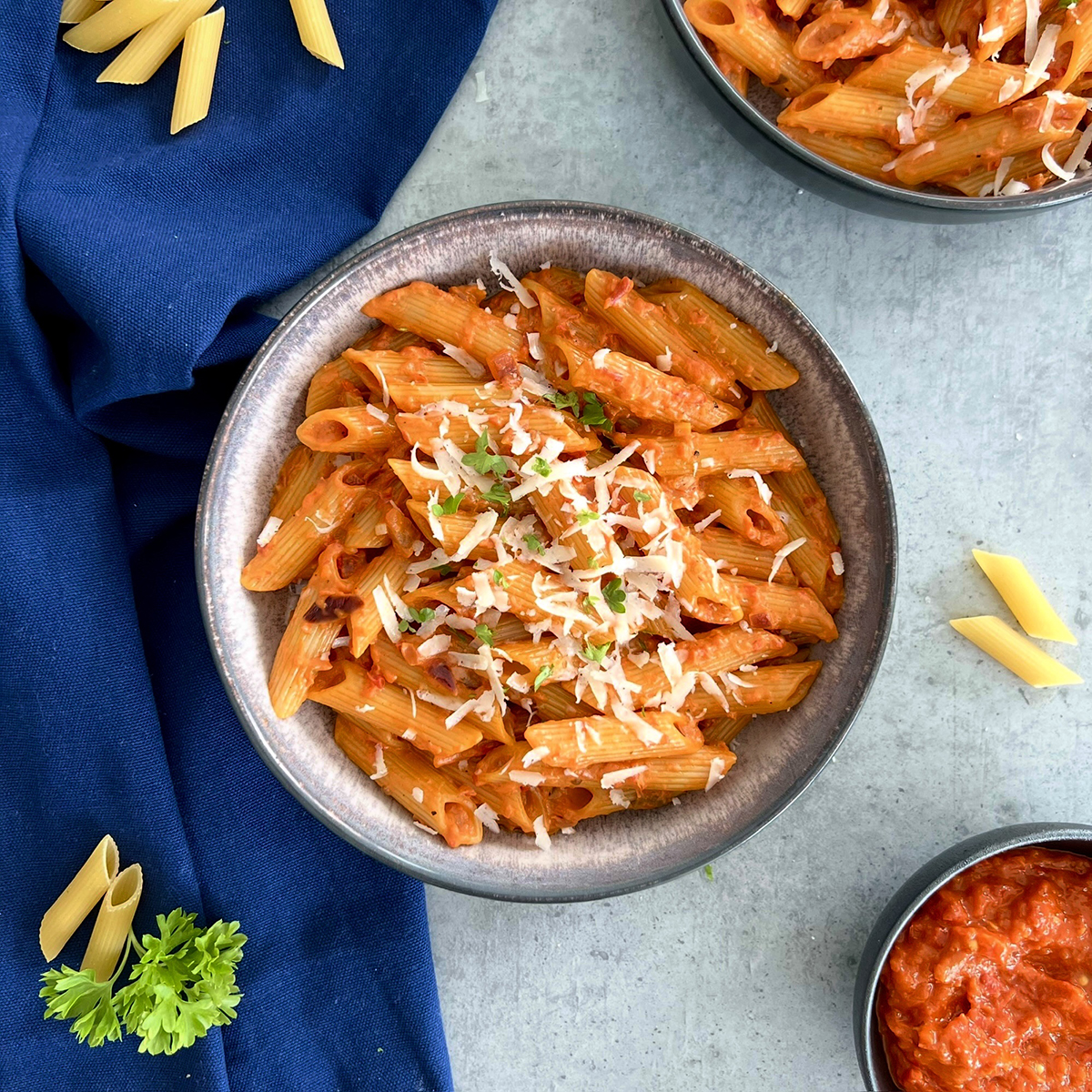 Das Bild zeigt die Pasta in einen tiefen, braunen Teller. Ein zweiter Teller und ein Schälchen Ajvar werden angeschnitten.