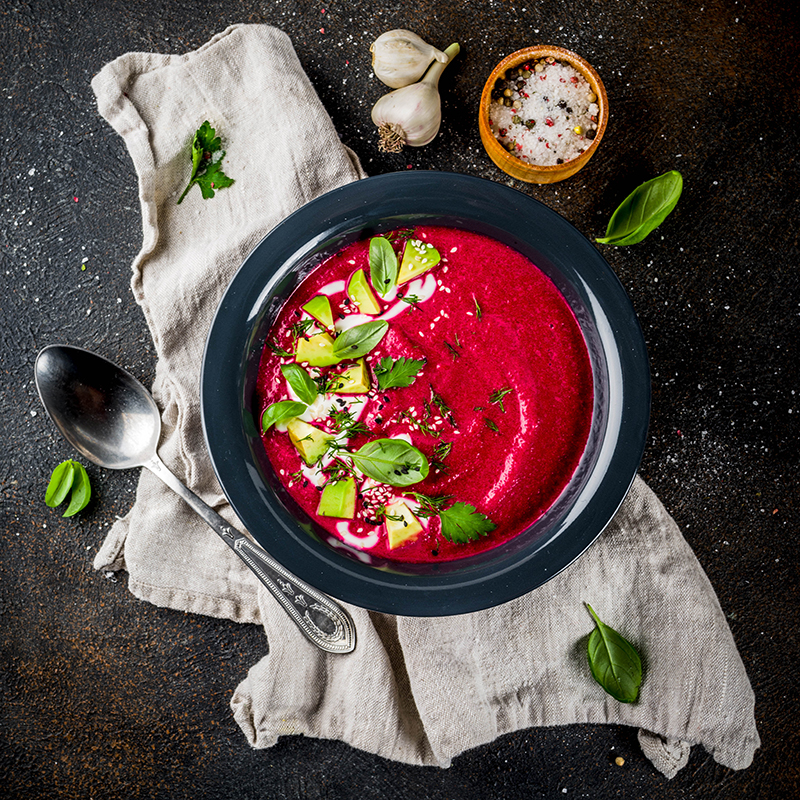 Rote Beete Suppe, die in einer schwarzen Schüssel garniert mit Basilikum auf einem grauem Leinentuch liegt.
