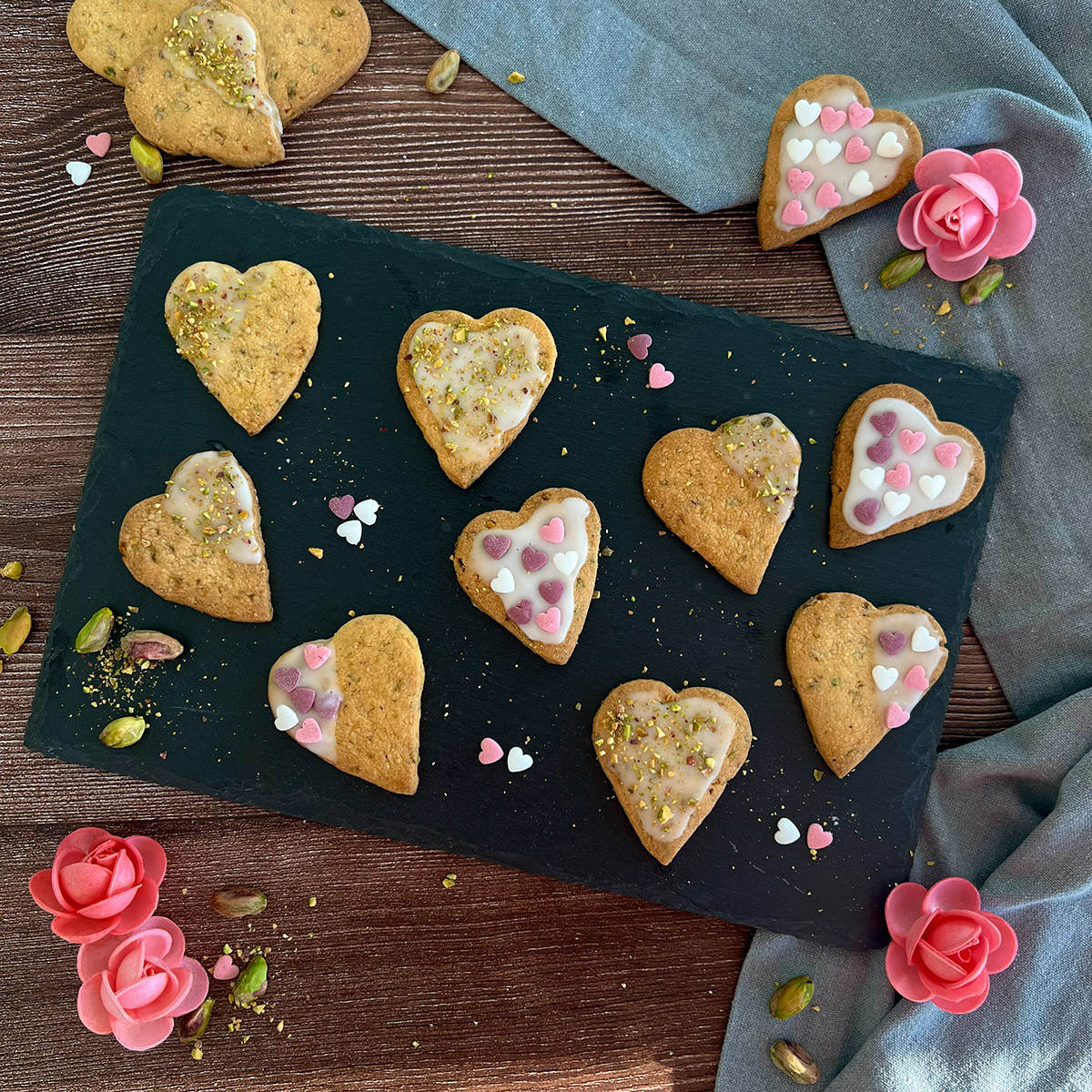 9 Kekse auf einer Schieferplatte, daneben weitere Kekse und Zuckerrosen