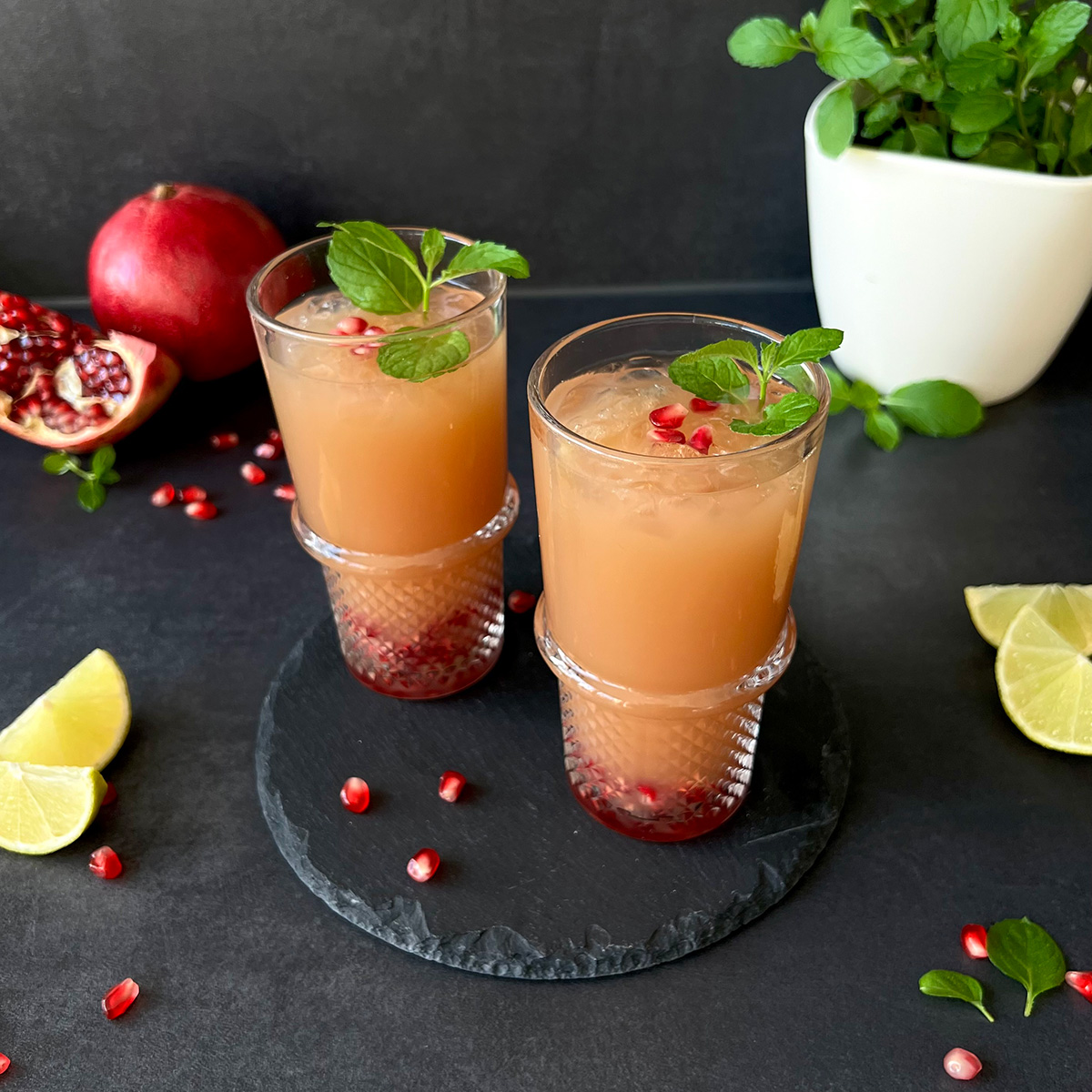 Das Bild zeigt 2 große Gläser gefüllt mit einem Mocktail. Es liegen Zitronen und Granatapfel daneben ebenso wie Kräuter.