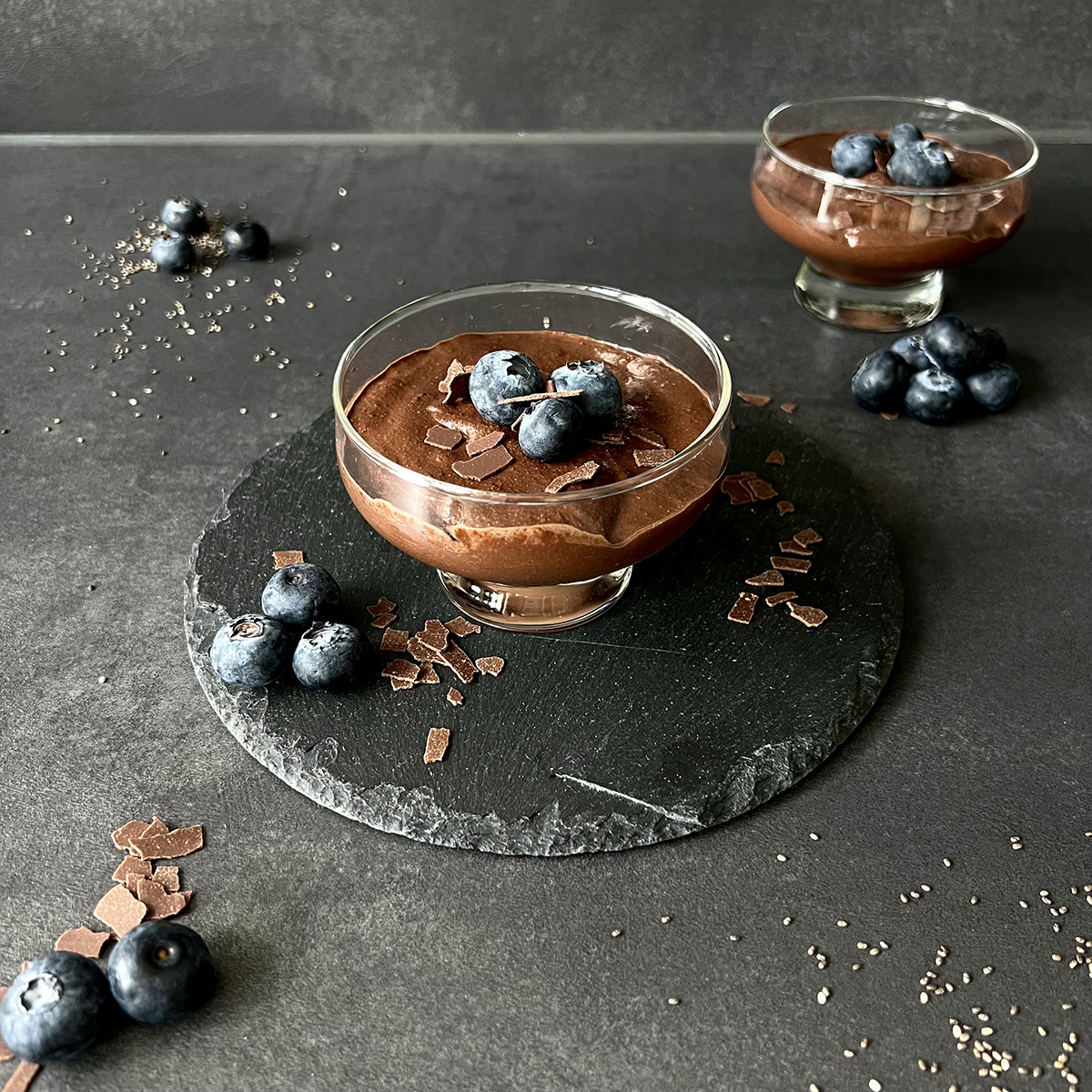 Zwei Dessert Gläser gefüllt mit Schokoladen Chia Mousse. Getoppt mit Blaubeeren und Schokoraspeln.