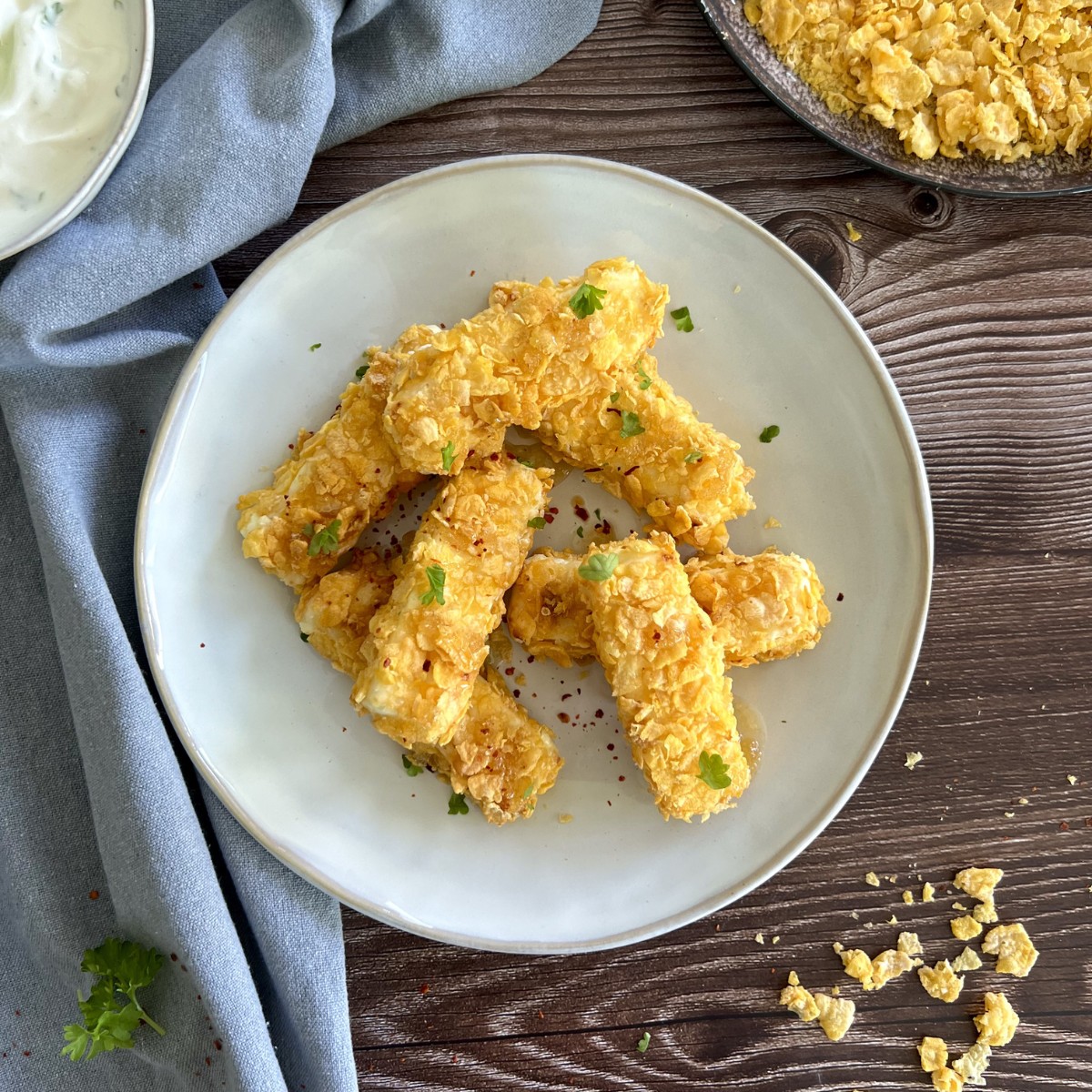 Das Bild zeigt panierte Feta Sticks verfeinert mit Petersilie. Neben dem Teller steht ein Dip.