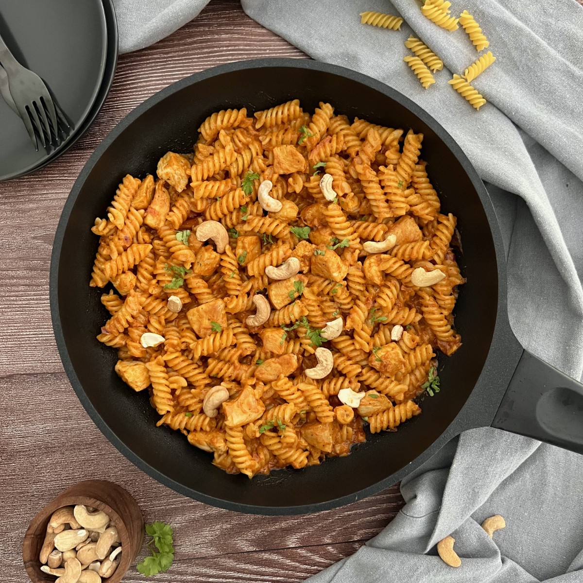 Das Bild zeigt eine Pfanne in der sich die Butter Chicken Pasta befindet, verfeinert mit Cashewkernen.