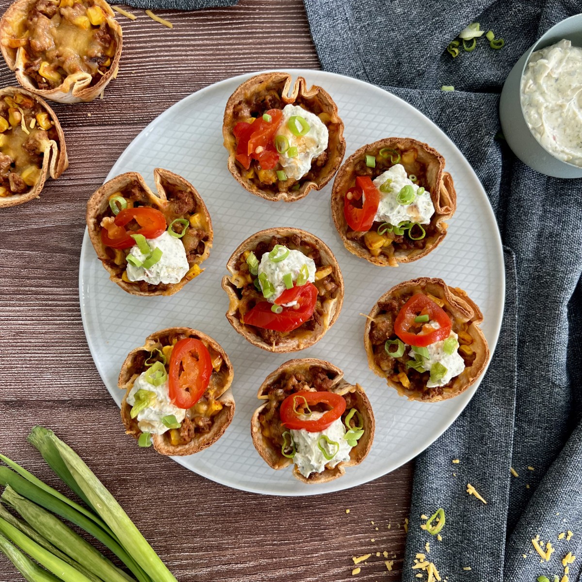 Sieben Cups sind auf einem flachen Teller. Die Cups sind mit Sour Cream, roten Jalapenos und Frühlingszwiebel getoppt.