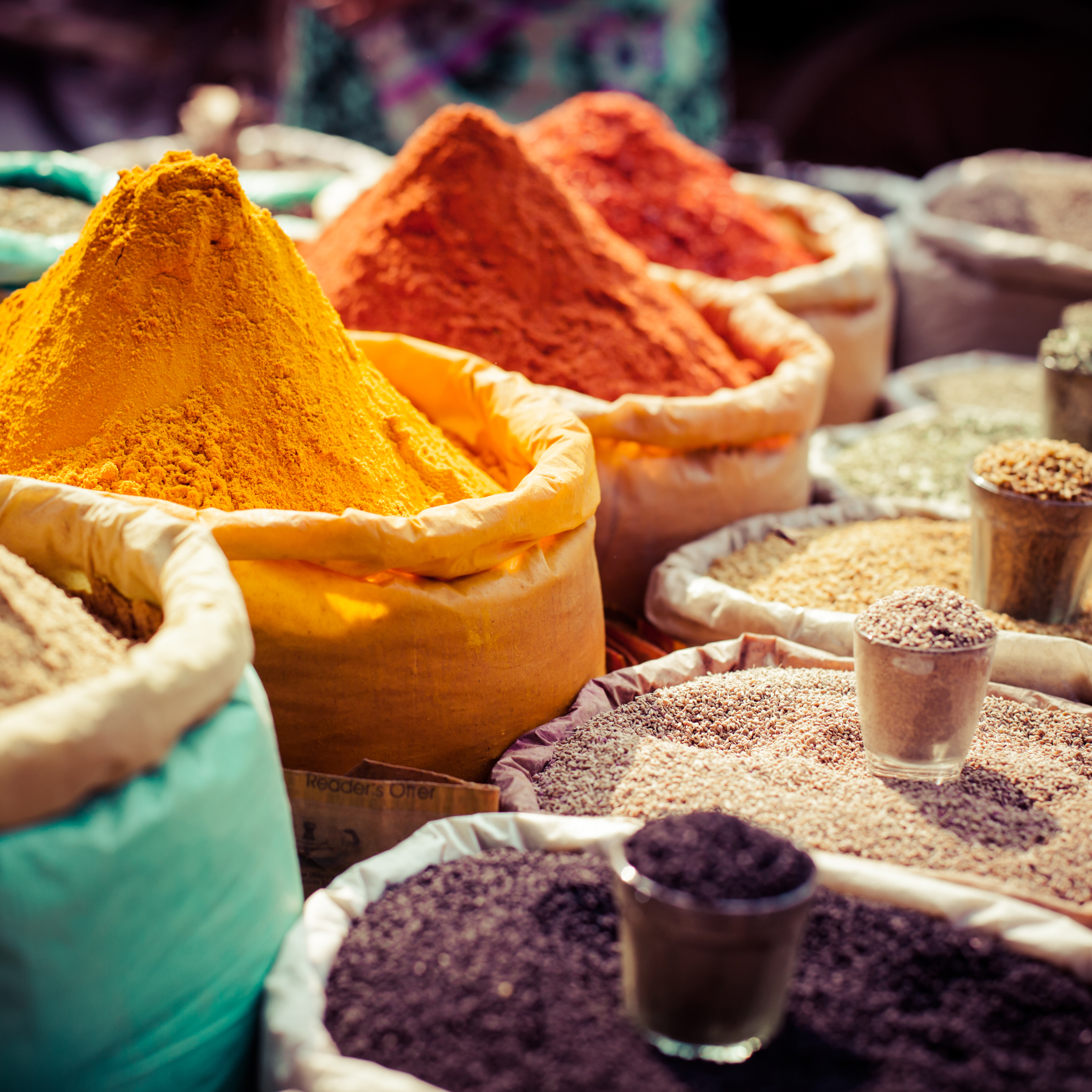 Mehrere bunte Säcke mit vielen Gewürzen, darunter gelbes Kurkumapulver und rotes Chili, auf einem Markt.