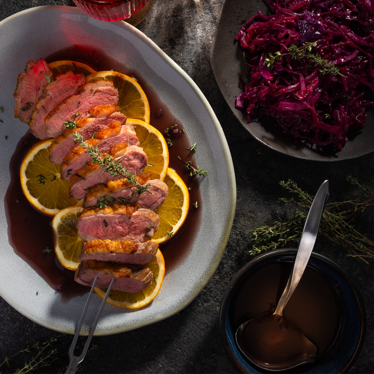 Ente auf Orangenscheiben auf einem Teller, daneben Rotkohl und sauce 