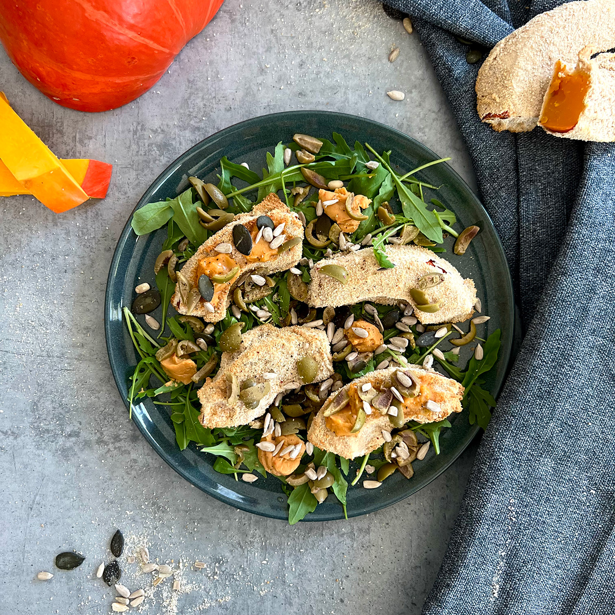 4 panierte Kürbis stücke auf Rucola auf einem Grauen Teller