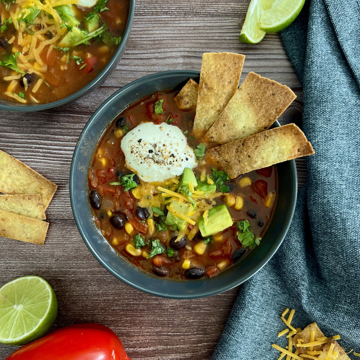 In einer Schale ist eine Tortilla Suppe getoppt mit knusprigen Tortilla Streifen, Sour Cream, Avocado und Käse.