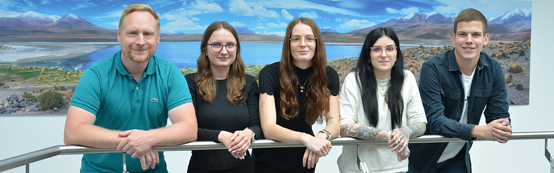 5 freundliche Menschen  vor einem Landschaftsbild.