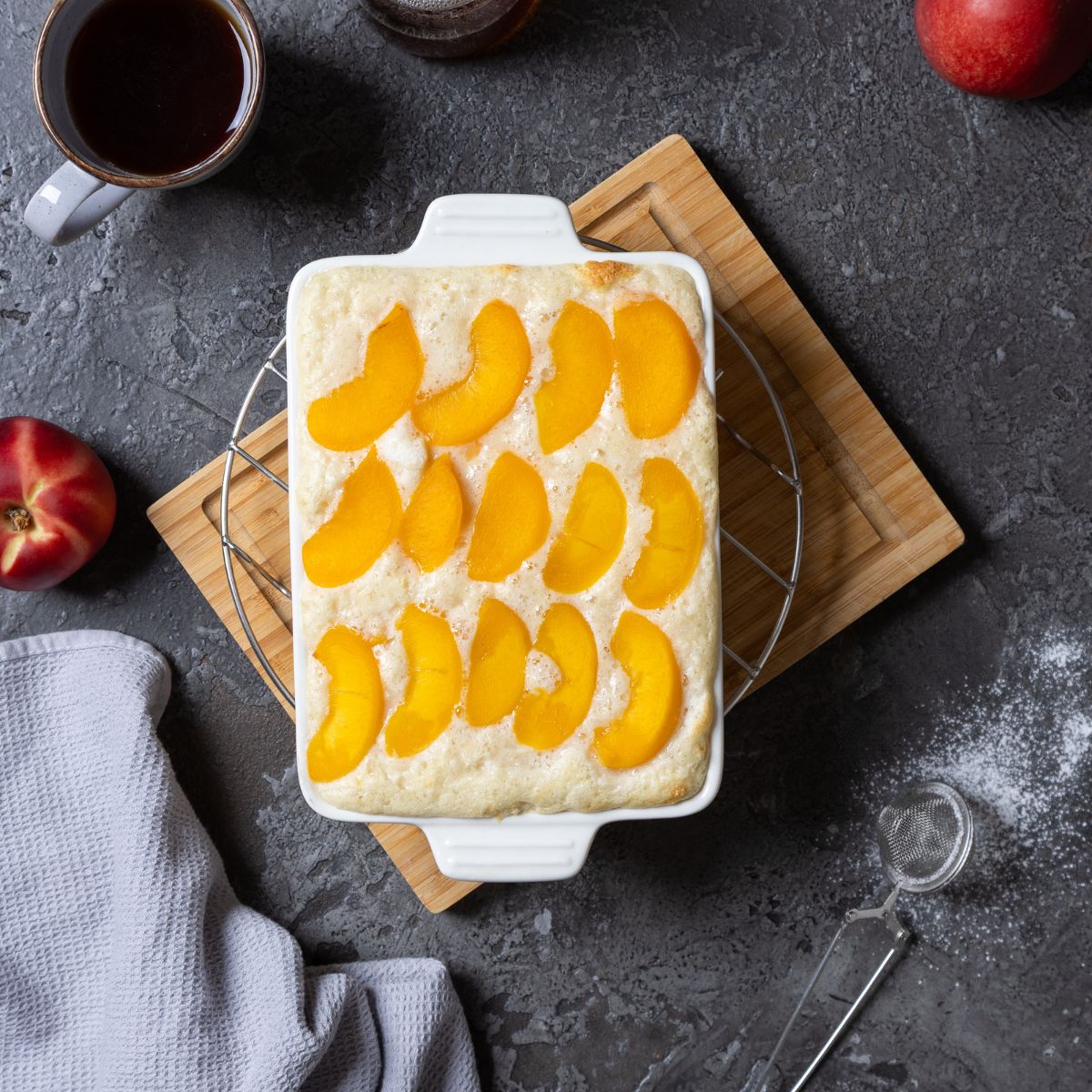 Dessert in einer Auflaufform, getoppt mit Pfirsichscheiben, daneben Pfirsiche