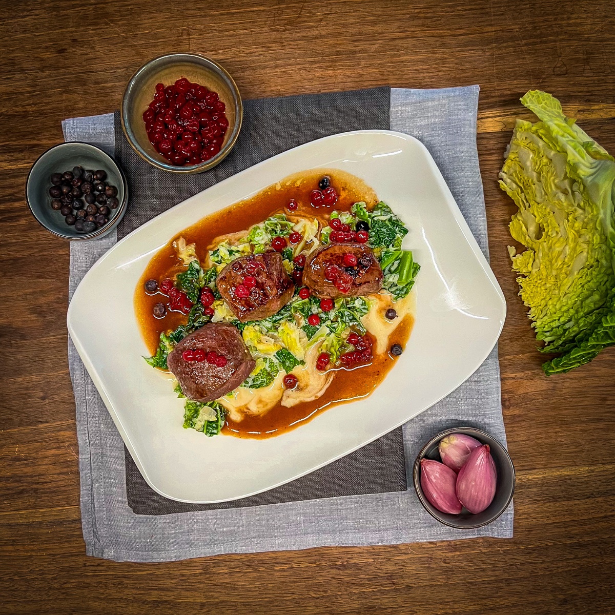 3 rehmedaillons mit Sauce und Wirsing auf einem Teller, daneben Wirsing und Zutaten